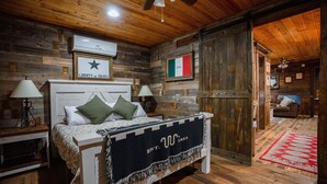 Een rustieke houten kamer met een bed, twee nachtkastjes, een plafondventilator en een deur met houten frame.