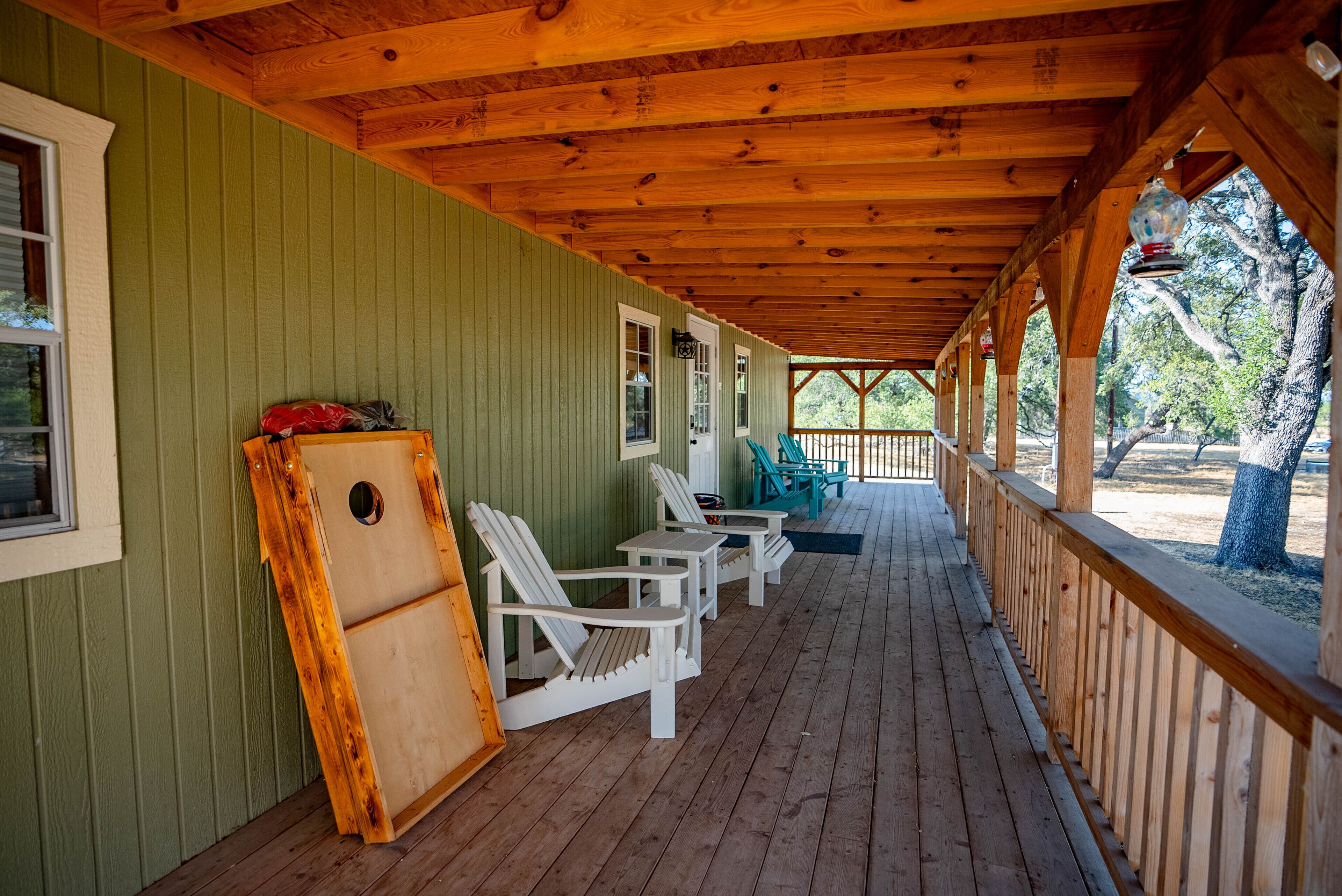 Een overdekte veranda met houten leuningen, witte Adirondack-stoelen en een houten tafel.