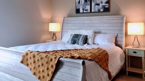 A neatly made bed with a white duvet and a brown throw blanket, flanked by two bedside tables with lamps, a ceiling fan, and abstract wall art above the bed. - Cheerful 4BR House Near Red Rocks & Mountains! (Littleton)