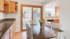 A modern kitchen with wooden cabinets, a granite countertop, and a dining area with a wooden table and white chairs. - Cheerful 4BR House Near Red Rocks & Mountains! (Littleton)