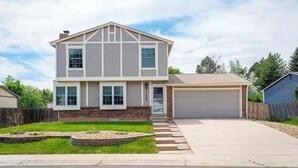 A two-story house with a garage, a front yard with a landscaped garden, and a clear sky. - Cheerful 4BR House Near Red Rocks & Mountains! (Littleton)