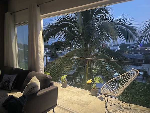 A balcony with a sofa, a chair, and potted plants.