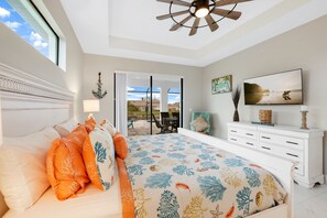 A bedroom with a bed, a ceiling fan, a TV, and a view of the outdoors.