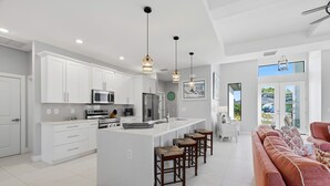 Uma cozinha moderna com armários brancos, uma ilha central com bancos e iluminação pendente.