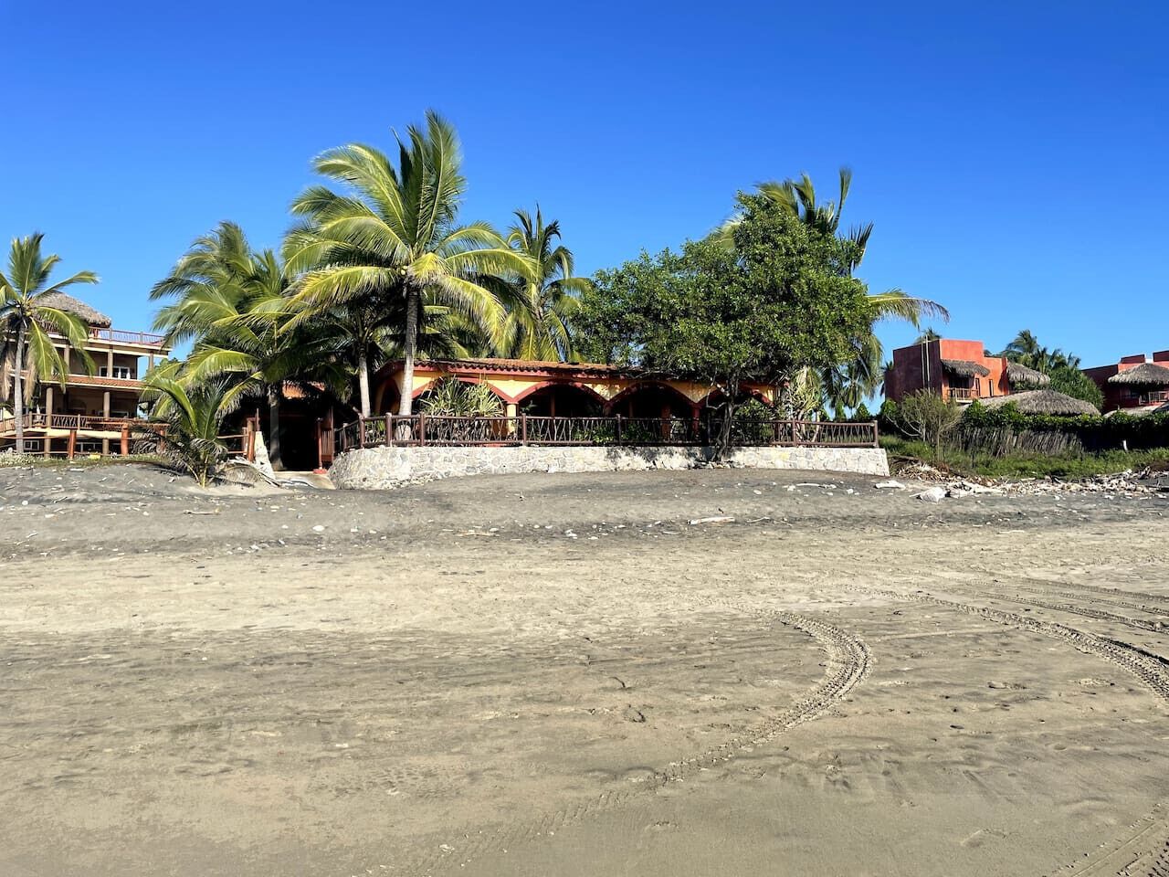 A sandy beach with a building featuring a thatched roof and palm trees.