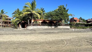 Una playa arenosa con un edificio de techo de paja y palmeras.