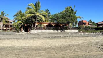 A sandy beach with a building featuring a thatched roof and palm trees.
