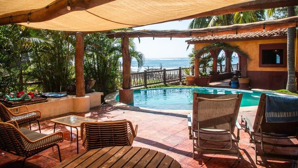 Zona de piscina con vista al océano, mobiliario de madera y un área de estar techada.