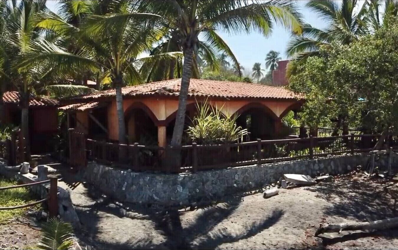 A rustic building with a tiled roof, surrounded by palm trees and a stone wall.
