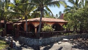 Un edificio rústico con techo de tejas, rodeado de palmeras y un muro de piedra.