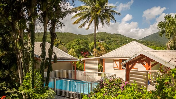 Un resort con piscina, rodeado de exuberante vegetación y palmeras, con montañas al fondo.