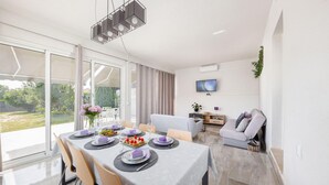 Un espace repas moderne avec une table dressée pour quatre personnes, un canapé et un téléviseur fixé au mur.