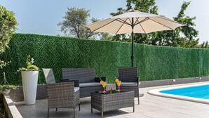Un espace extérieur aménagé avec des meubles en osier, une table avec des boissons et une piscine en arrière-plan.