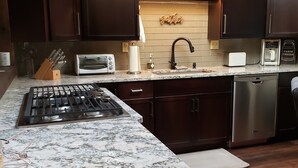 Una cocina moderna con gabinetes de madera oscura, encimera de granito, estufa a gas, horno empotrado, lavaplatos y lavavajillas.