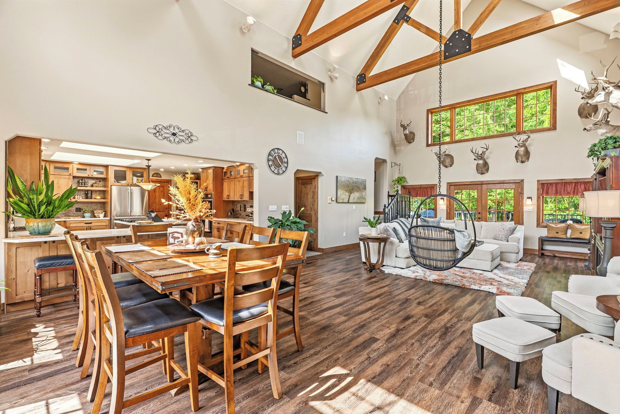 A spacious living area with a high ceiling, wooden beams, a dining table with chairs, a hanging chair, and a sofa.