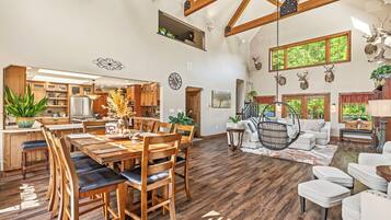 A spacious living area with a high ceiling, wooden beams, a dining table with chairs, a hanging chair, and a sofa.