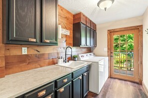 A kitchen with wooden paneling, a sink, cabinets, and a view of the outdoors through a glass door. - The Peaceful Hidden House, Bed & Breakfast (Castle Rock)