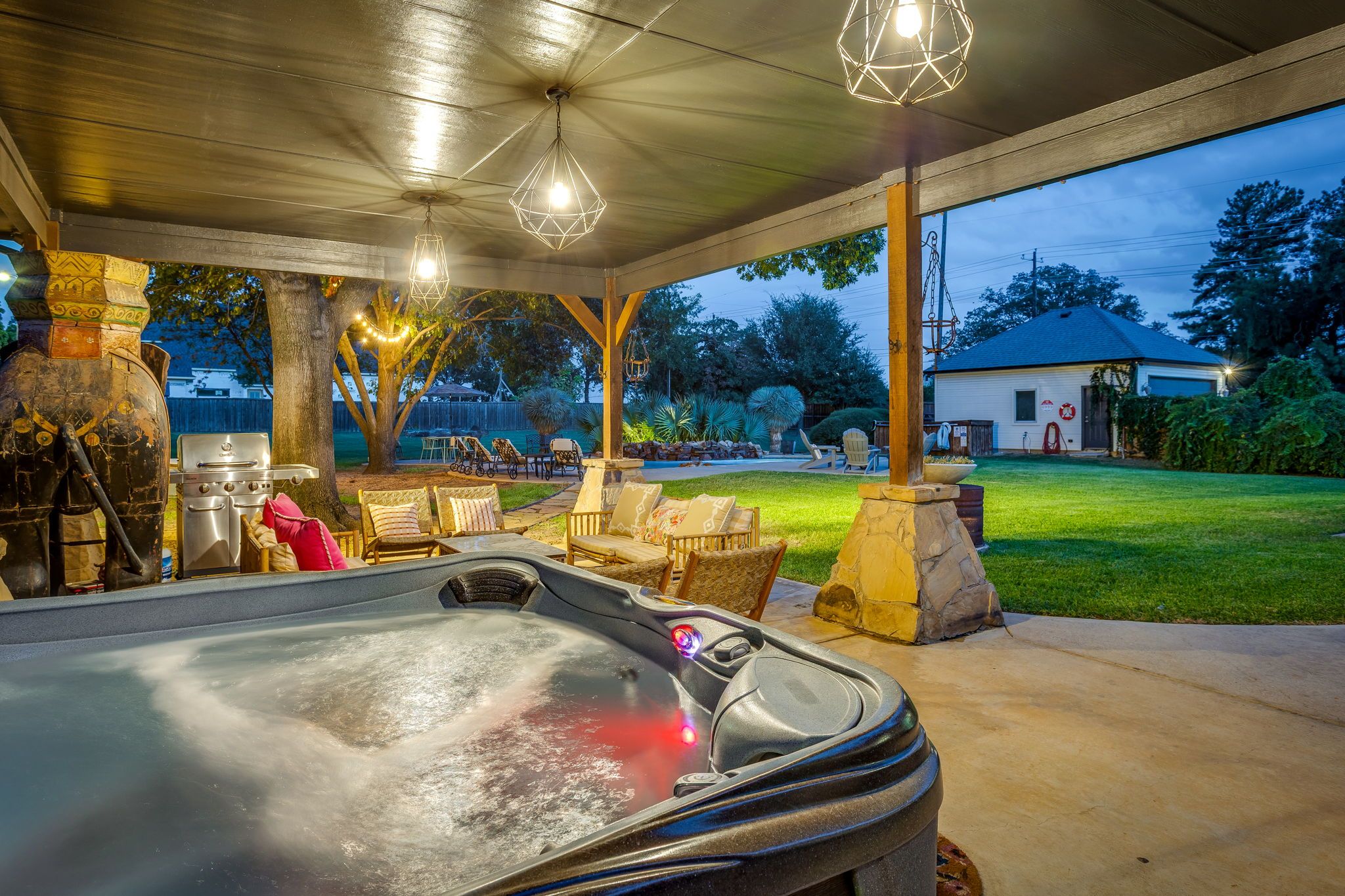 A hot tub with a stone surround, outdoor seating, and string lights.