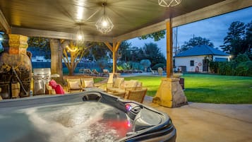 A hot tub with a stone surround, outdoor seating, and string lights.