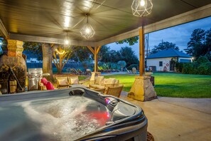 A hot tub with a stone surround, outdoor seating, and string lights.