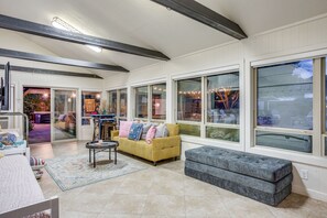 A spacious living room with a large window, a yellow sofa, and a grey bench.