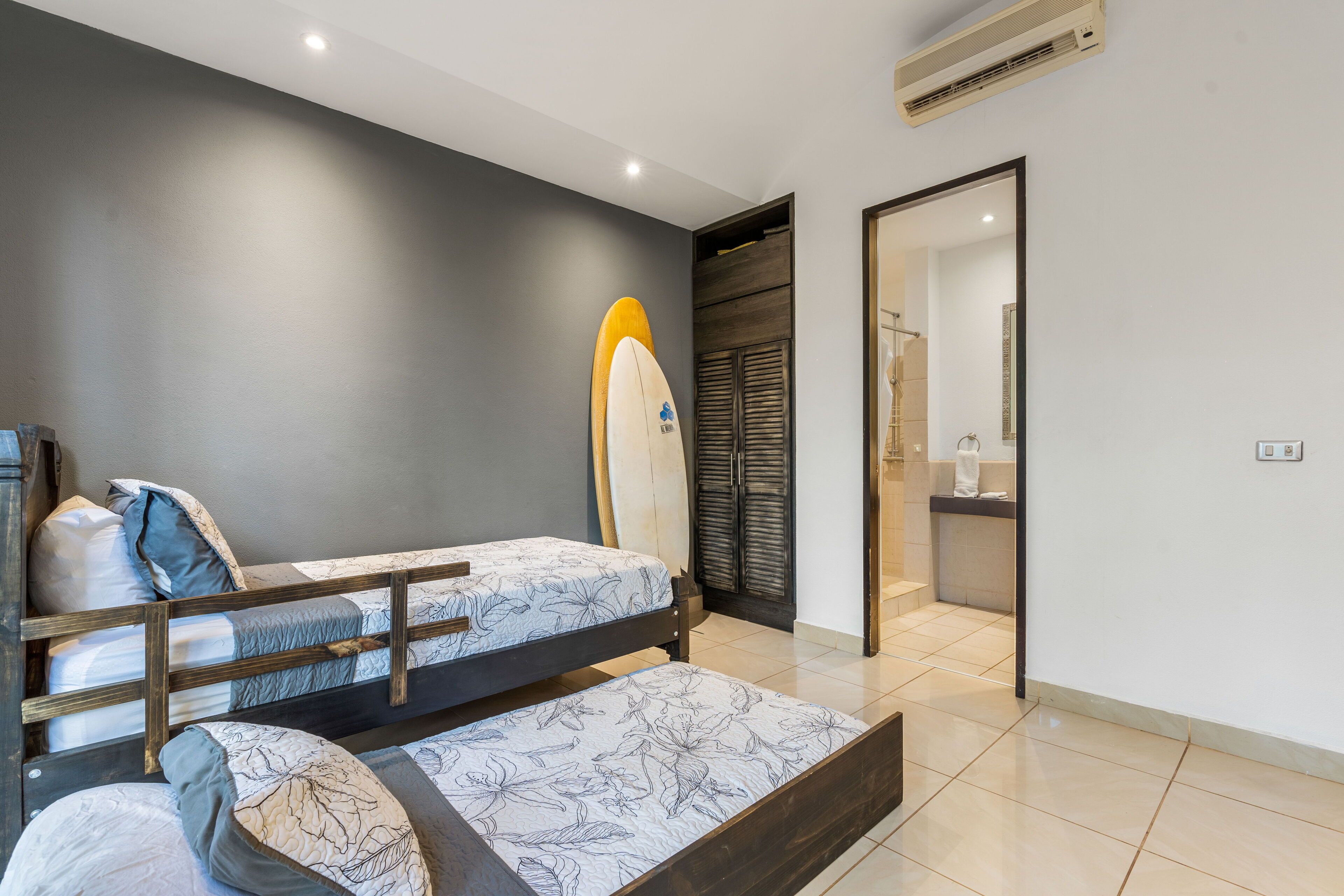 A bedroom with two beds, a wardrobe, and a bathroom visible through an open door.