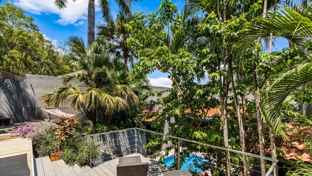 Terraza en la azotea con mobiliario de mimbre, piscina y exuberante vegetación tropical.