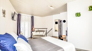 Hotellihuone, jossa on sänky, tuoli, pieni pöytä, peili ja ikkuna, jossa on verhot.