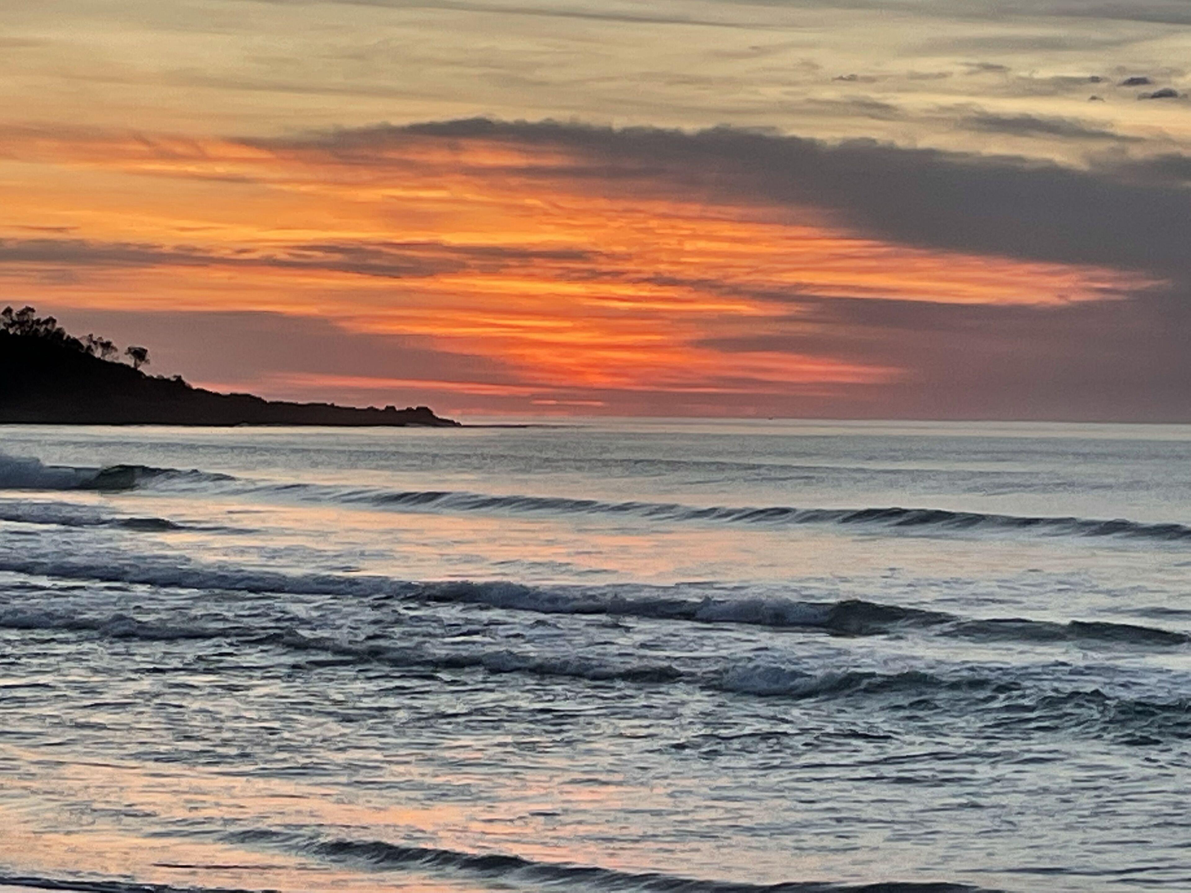 A coastal sunset with waves and a distant shoreline.