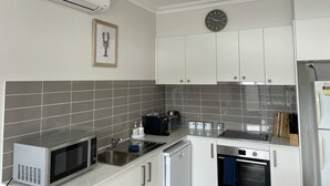 A modern kitchen with white cabinets, a stainless steel sink, a microwave, a toaster, and a clock on the wall. - Two bedroom villa with private courtyard, a short walk to Manyana Beach. (Manyana)