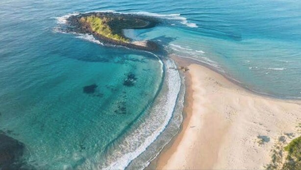 An aerial view of a beach with clear turquoise waters, a sandy shore, and a small island with vegetation. - Two bedroom villa with private courtyard, a short walk to Manyana Beach. (Manyana)