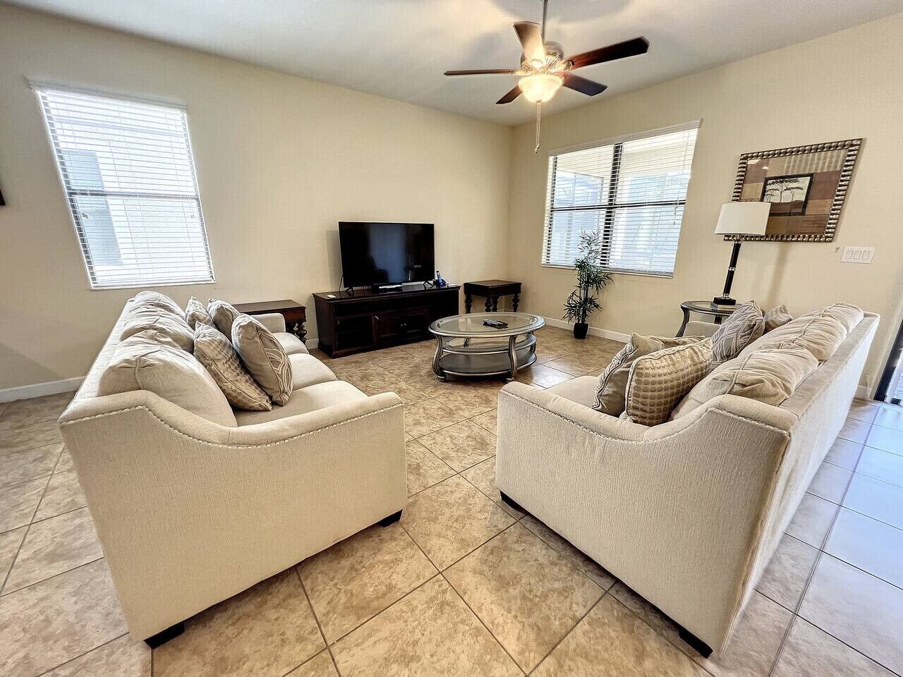 A living room with two beige sofas, a TV, a ceiling fan, and a coffee table.