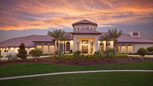 A large, two-story house with a central courtyard, surrounded by a well-maintained lawn and palm trees.