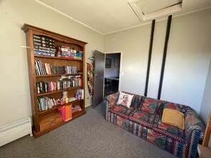 Ein Wohnzimmer mit einer großen, hölzernen Bücherwand, voll mit Büchern und DVDs, einem gemusterten Sofa und einer Heizung.