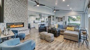A spacious living room with a fireplace, modern furniture, and a kitchen in the background. - Lake Escape w/ Private Dock & Spa-like amenities (Iron Mountain)