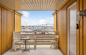 Een houten balkon met een tafel en twee stoelen, met uitzicht op een jachthaven met boten en een brug op de achtergrond.