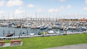 En marina med mange både i havnen, et grønt område med picnicborde, og en bro i baggrunden.