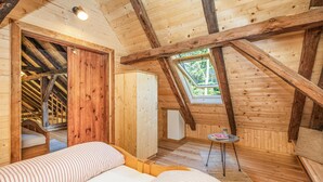 Ein gemütliches Schlafzimmer im Dachgeschoss mit Holzbalken, einem Oberlicht und einem Bett mit gestreifter Bettwäsche.