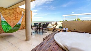 Een balkon met een hangmat, een houten bank, een tafel met stoelen en uitzicht op de oceaan.