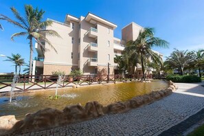Un bâtiment moderne doté de nombreux balcons, d’une allée pavée et d’un élément décoratif aquatique.