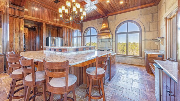 A spacious kitchen with a large island, wooden bar stools, and a stone backsplash. - Castle at Fort Morgan- Dreams do come true! (Gulf Shores)
