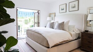 Un dormitorio con cama, mesitas de noche, una ventana con vistas y una puerta que da a un área exterior.