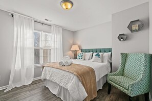 Una camera da letto ordinata con un letto, una sedia, una lampada e una finestra con tende.