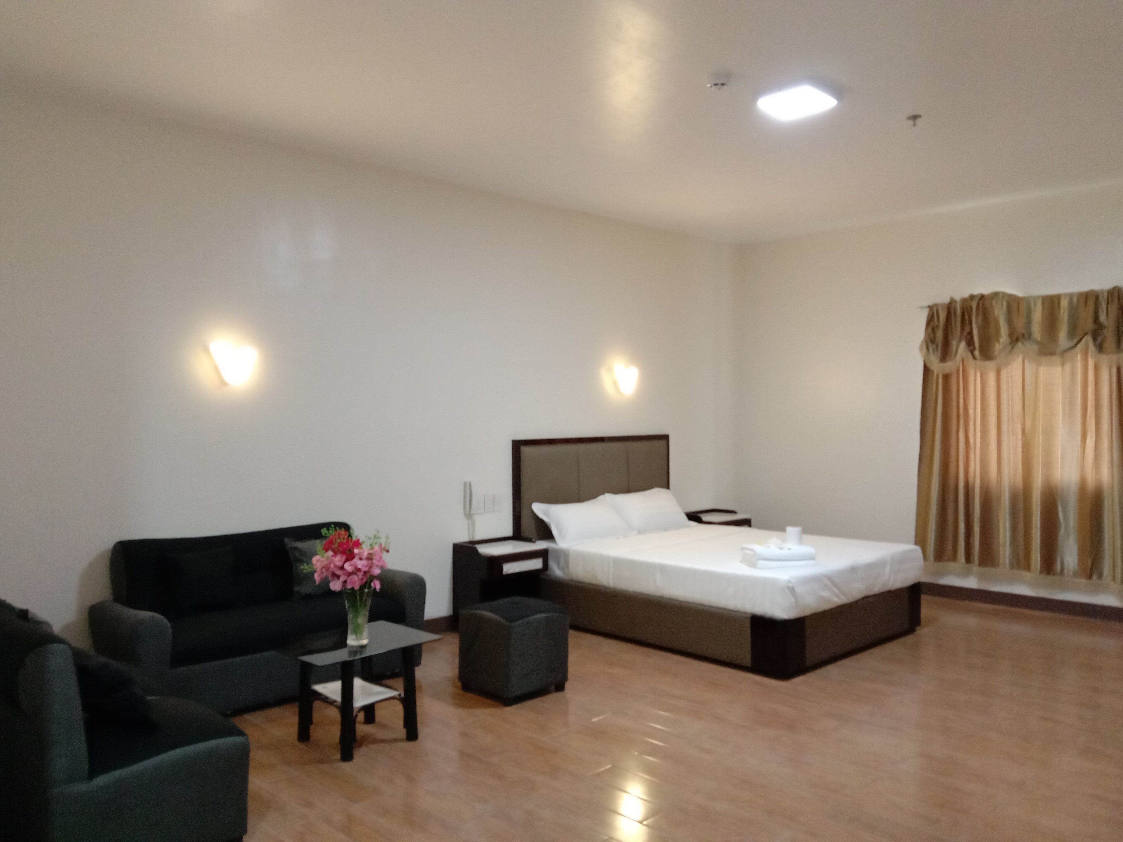 Una habitación de hotel con una cama, un sofá, una mesita con un florero y una mesita de noche.
