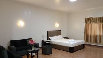 Una habitación de hotel con una cama, un sofá, una mesita con un florero y una mesita de noche.