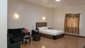 A hotel room with a bed, a sofa, a small table with a vase of flowers, and a window with curtains.