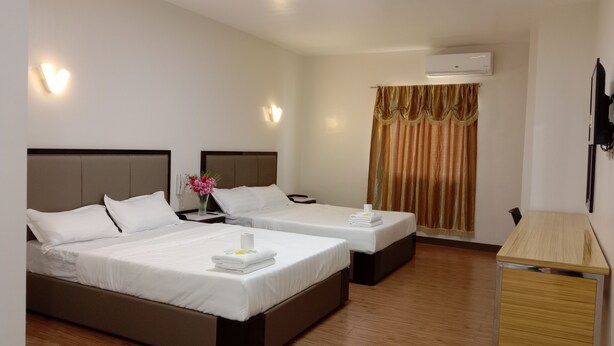 A hotel room with two beds, a wooden floor, a desk, and an air conditioning unit. - Meaco Royal Hotel- Lucena (Lucena)