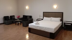 A hotel room with a large bed, two armchairs, a small table with a vase of flowers, and two bedside tables with lamps. - Meaco Royal Hotel- Lucena (Lucena)