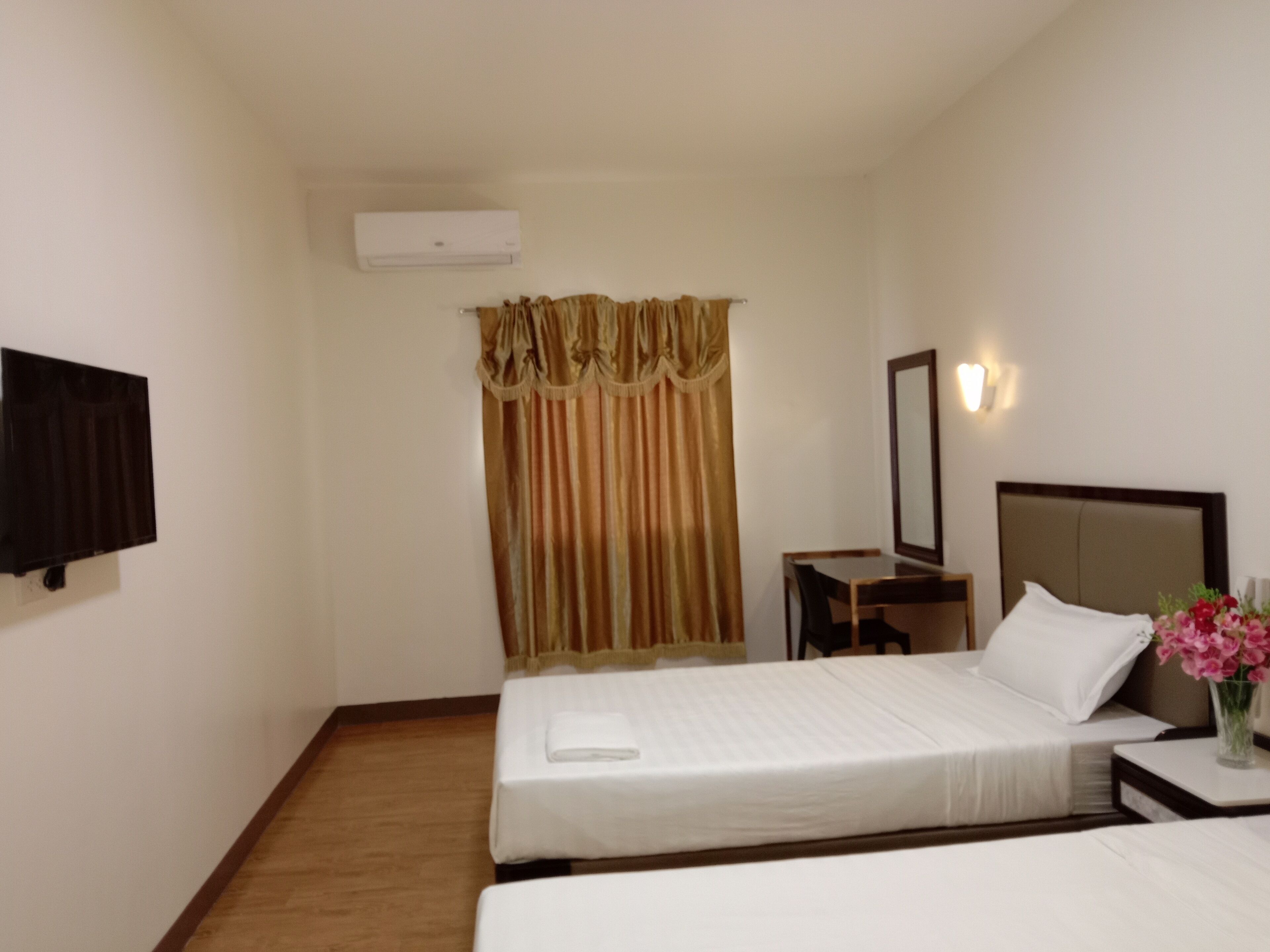 Quarto de hotel com duas camas, uma TV de tela plana, mesa de cabeceira com um vaso de flores e ar-condicionado fixado na parede.