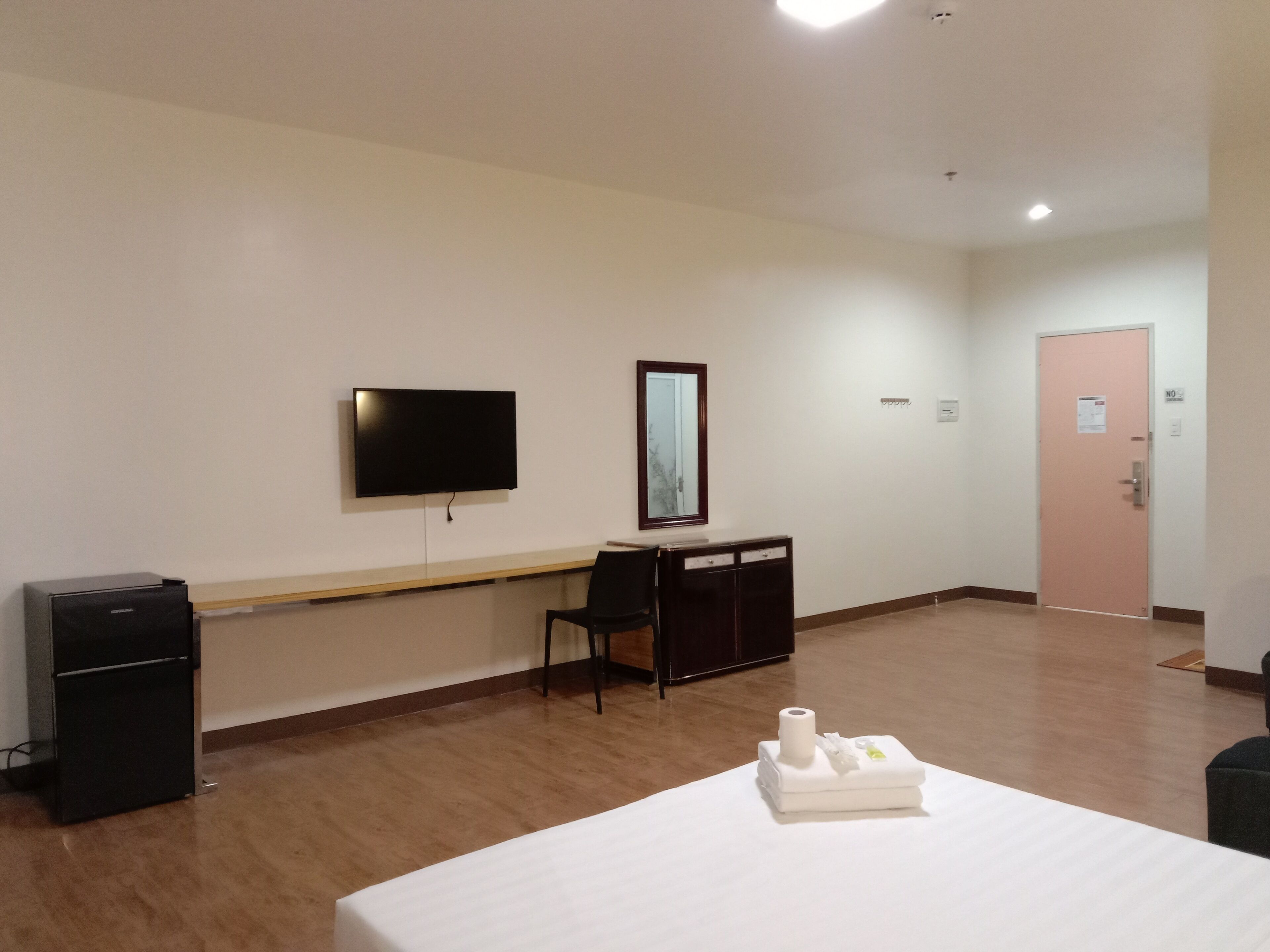 A hotel room with a bed, a desk with a chair, a television, and a door.
